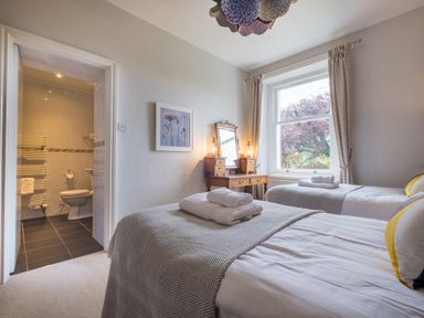 A bedroom with two single beds with towels on them a wooden dressing table and a window showing trees at Swinside Lodge in Newlands Valley near Keswick
