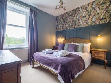 A bedroom with a double bed purple bedding wooden bedside tables and a window with curtains at Swinside Lodge in Newlands Valley near Keswick