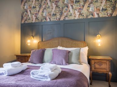 A bedroom with a bed with purple and green pillows and folded white towels on a purple blanket at Swinside Lodge in Newlands Valley near Keswick