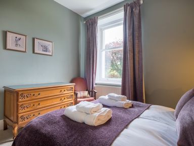 A bedroom with a wooden dresser two framed animal pictures a window with curtains and a bed with towels on a purple throw at Swinside Lodge in Newlands Valley near Keswick