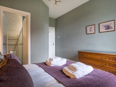 A bedroom with a bed, folded towels on a purple runner, a wooden dresser, animal artwork on the wall, and a view into a bathroom at Swinside Lodge in Newlands Valley near Keswick