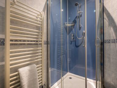 A bathroom shower cubicle with blue walls a showerhead and a white towel on a rail at Swinside Lodge in Newlands Valley near Keswick