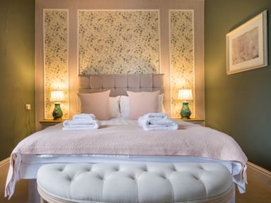 A bedroom with a bed with beige pillows and folded towels on top two lamps on bedside tables and floral wallpaper at Swinside Lodge Newlands Valley near Keswick