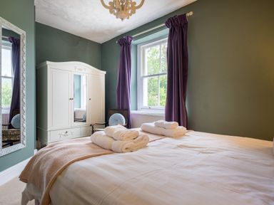 A bedroom with bed linens and towels on the bed a white wardrobe purple curtains and a chair at Swinside Lodge in Newlands Valley near Keswick
