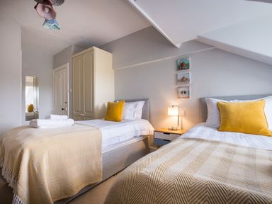 A bedroom with two single beds beige bedspreads yellow cushions a wardrobe and a bedside table with a lamp at Swinside Lodge in Newlands Valley near Keswick