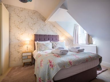 A bedroom with a double bed floral quilt two bedside tables with lamps and a window with curtains at Swinside Lodge Newlands Valley near Keswick
