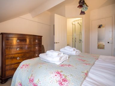 A bedroom with a wooden dresser a bed with floral bedding and white towels two doors one leading to a shower room at Swinside Lodge in Newlands Valley near Keswick