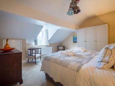 A bedroom with a bed with folded towels on it a wardrobe two chairs a chest of drawers and a window at Swinside Lodge Newlands Valley near Keswick