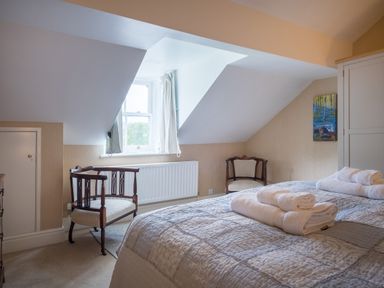 A bedroom with a bed covered in a quilt and towels, two wooden chairs, a window with curtains, a wardrobe, and a painting on the wall at Swinside Lodge in Newlands Valley near Keswick