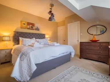 A bedroom with a large bed with folded towels bedside tables with lamps a wooden dresser and an oval mirror at Swinside Lodge Newlands Valley near Keswick