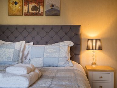 A bedroom with a gray upholstered headboard pillows a bedside table with a lamp and folded towels at Swinside Lodge in Newlands Valley near Keswick