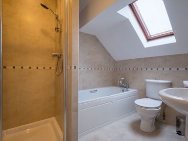 A bathroom with a shower, bathtub, toilet, sink, and skylight window at Swinside Lodge in Newlands Valley near Keswick