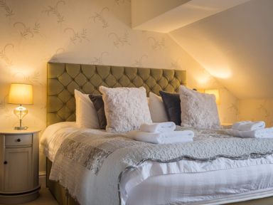 A bedroom with a large bed with pillows and folded towels on it and bedside tables with lamps at Swinside Lodge in Newlands Valley near Keswick