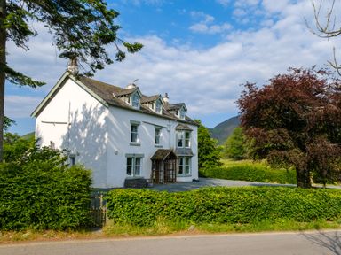 A white two-story house with dormer windows surrounded by greenery and trees at Swinside Lodge in Newlands Valley near Keswick
