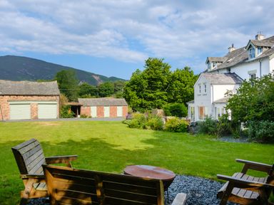 A garden with wooden benches and a fire pit surrounded by a lawn and buildings at Swinside Lodge in Newlands Valley near Keswick