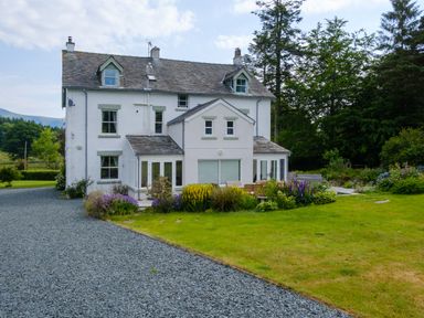 A white multi-story house with a gravel driveway and garden with flowers at Swinside Lodge in Newlands Valley near Keswick