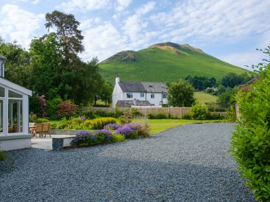 A gravel driveway with flower beds and garden furniture by a white house with a green hill in the background at Swinside Lodge in Newlands Valley near Keswick