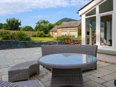 An outdoor patio with a glass top round table and wicker chairs near a house and garden at Swinside Lodge Newlands Valley near Keswick