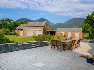 An outdoor patio with wooden table and chairs next to stone steps and brick buildings with green doors at Swinside Lodge in Newlands Valley near Keswick