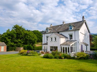 A large white house with an outdoor seating area surrounded by a garden and trees at Swinside Lodge in Newlands Valley near Keswick