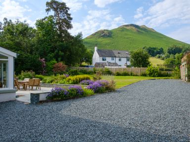 A garden with patio furniture a gravel driveway purple flowers and a green hill behind a white house at Swinside Lodge Newlands Valley near Keswick