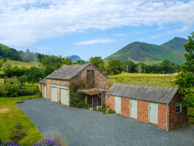 A brick garage and outbuilding with green doors and a gravel driveway in a rural setting at Swinside Lodge in Newlands Valley near Keswick