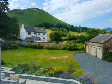 A garden with lawn and flower beds next to a gravel driveway leading to garages and a white house with hills in the background at Swinside Lodge in Newlands Valley near Keswick