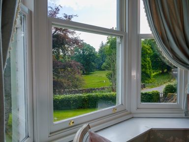A view through a bay window showing trees grass a stone wall and a road at Swinside Lodge in Newlands Valley near Keswick