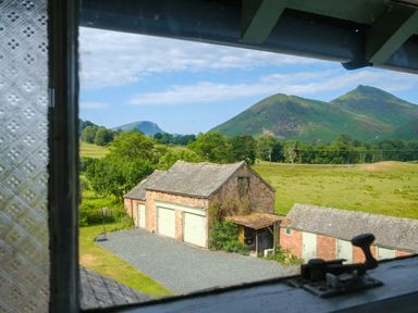 A view from a window showing brick garages with green doors and a grassy field with hills and trees in the background at Swinside Lodge in Newlands Valley near Keswick