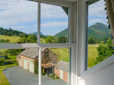 A rural view through a window showing a brick garage, green fields, trees, and hills at Swinside Lodge in Newlands Valley near Keswick