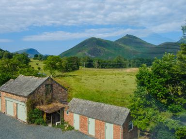 A rural scene with brick outbuildings and green fields with hills in the background at Swinside Lodge in Newlands Valley near Keswick