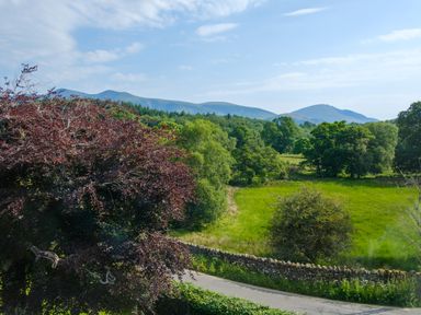 A rural landscape with trees grass a stone wall and mountains in the background at Swinside Lodge in Newlands Valley near Keswick