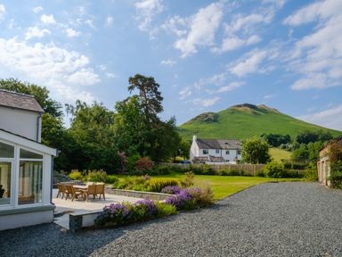 A garden with patio furniture and flower beds next to a white house with a green hill in the background at Swinside Lodge in Newlands Valley near Keswick