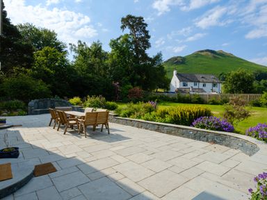 An outdoor patio with a wooden table and chairs surrounded by flowers and a house near a hill at Swinside Lodge Newlands Valley near Keswick