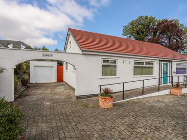 Exterior of a white building with a red tiled roof and a blue door with a driveway leading to a garage at Haddef Penmaenmawr in Penmaenmawr