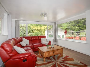 A living room with a red sectional sofa and wooden coffee table by large windows at Haddef Penmaenmawr in Penmaenmawr