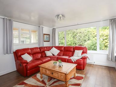 A living room with a red corner sofa wooden coffee table and large windows at Haddef Penmaenmawr in Penmaenmawr