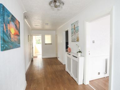 A hallway with wooden floor and white walls with paintings and a small radiator cover at Haddef Penmaenmawr in Penmaenmawr