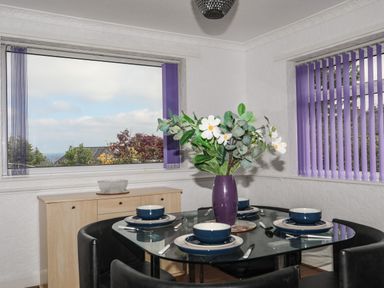 A dining room with a glass table set for four and purple vertical blinds at Haddef Penmaenmawr in Penmaenmawr