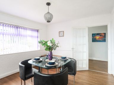 A dining room with a glass table set for four people black chairs a purple vase with flowers and a window with purple blinds at Haddef Penmaenmawr in Penmaenmawr