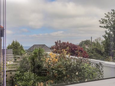 A garden with various plants and bushes with houses and the sea in the background at Haddef Penmaenmawr in Penmaenmawr