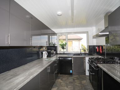 A kitchen with grey cabinets a countertop a sink a window and appliances at Haddef Penmaenmawr in Penmaenmawr