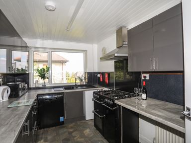 A kitchen with black oven dishwasher and cabinets next to a window at Haddef Penmaenmawr in Penmaenmawr