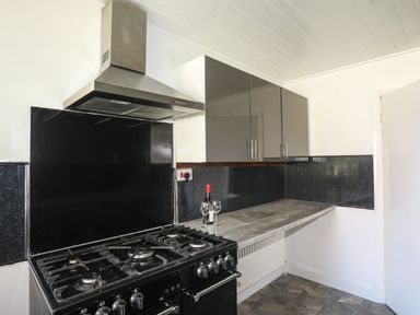 A kitchen with a gas stove a stainless steel extractor fan wall cabinets and a countertop with a bottle of wine and two glasses at Haddef Penmaenmawr in Penmaenmawr