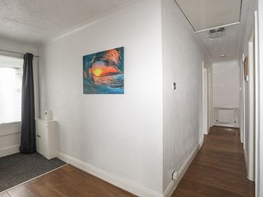 A hallway with wooden flooring a white wall with a wave painting and a window with dark curtains at Haddef Penmaenmawr in Penmaenmawr