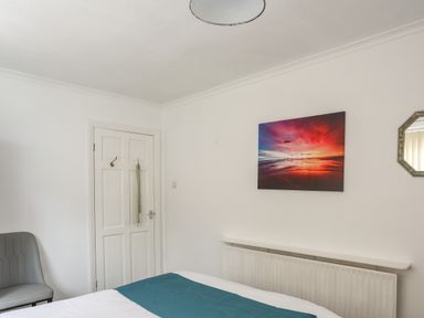 A bedroom with a bed a gray chair a door a radiator and a sunset picture on the wall at Haddef Penmaenmawr in Penmaenmawr