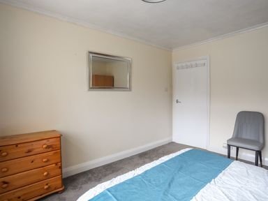 A bedroom with a wooden dresser gray chair white door and a bed with a blue cover at Haddef Penmaenmawr in Penmaenmawr
