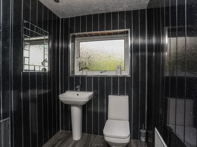 A bathroom with a pedestal sink a toilet a window with decorative glass and a mirror on the wall at Haddef Penmaenmawr in Penmaenmawr