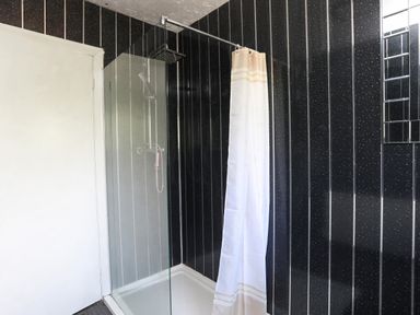 A bathroom with a black shower area with vertical lines and a white shower curtain at Haddef Penmaenmawr in Penmaenmawr