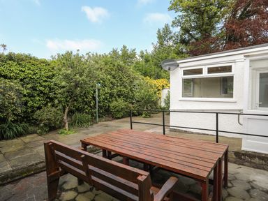 Outdoor patio area with wooden table and bench near white building and garden at Haddef Penmaenmawr in Penmaenmawr